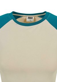 Ekologiška medvilninė marškinėlių sukreminės spalvos kūnu ir teal spalvos rankovėmis. Apvalus iškirpimas su siuvinėjimo detalėmis, minkšta tekstūra, XS dydis.