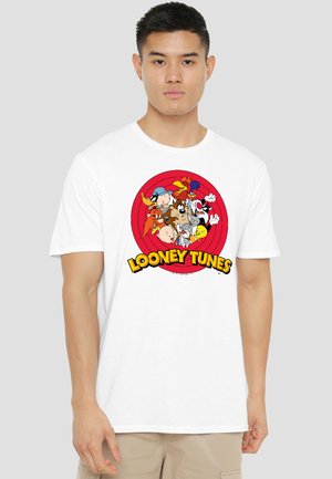 Young man wearing a white T-shirt featuring Looney Tunes characters clustered inside a red circle with "Looney Tunes" text below.