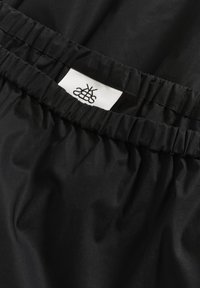 Svart tyg med en slät textur och elastisk midjeband; har en vit etikett med svart logotyp och text.