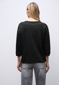 Felpa nera con maniche a tre quarti, vestibilità rilassata e dettagli a costine sulle spalle, abbinata a jeans grigi chiari.