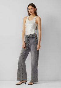 Jeans gris à jambe large avec une taille haute, une fermeture à bouton classique et des poches avant. Associé à un top à fines côtes ajusté et des sandales à talons.