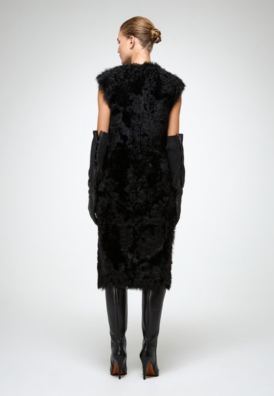 Gilet in finta pelliccia nera con design senza maniche, abbinato a lunghi guanti di pelle nera e stivali alti fino alla coscia con tacco, texture liscia.