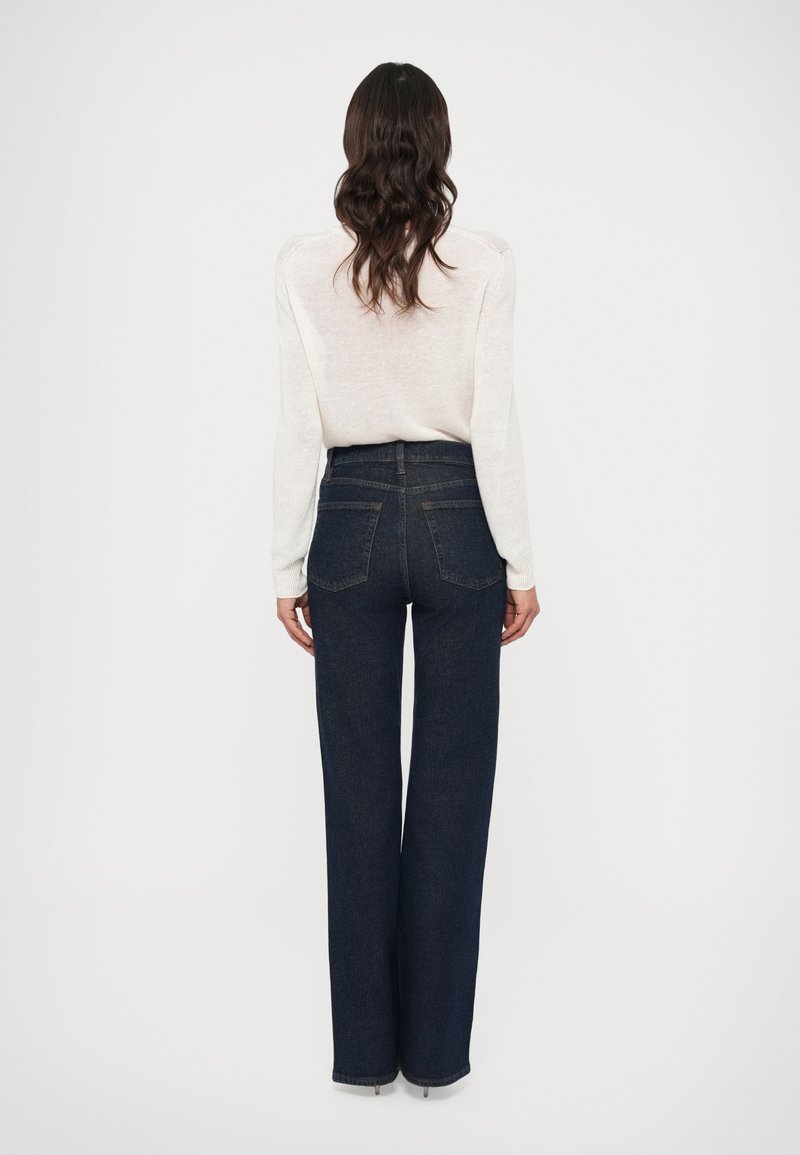 Dunkelblaue Jeans mit hoher Taille und geradem Bein, mit klassischer Denim-Struktur und zwei Gesäßtaschen. Lässiges Strickoberteil.