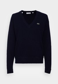 Navy blue sweater with a V-neck, made of soft fabric. Features ribbed cuffs and hem, and a small green Lacoste logo on the left chest.