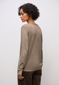 Pull beige à manches longues avec un col rond et des poignets côtelés, porté sur un pantalon marron foncé, vu de dos. Texture douce.