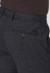 Dark gray trousers with a textured check pattern. Features a button closure and a small pocket detail on the back. Clean, tailored shape.