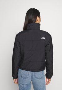 Black puffer jacket with a high collar, horizontal stitching, and a small white logo on the upper back. Smooth texture and lightweight design.