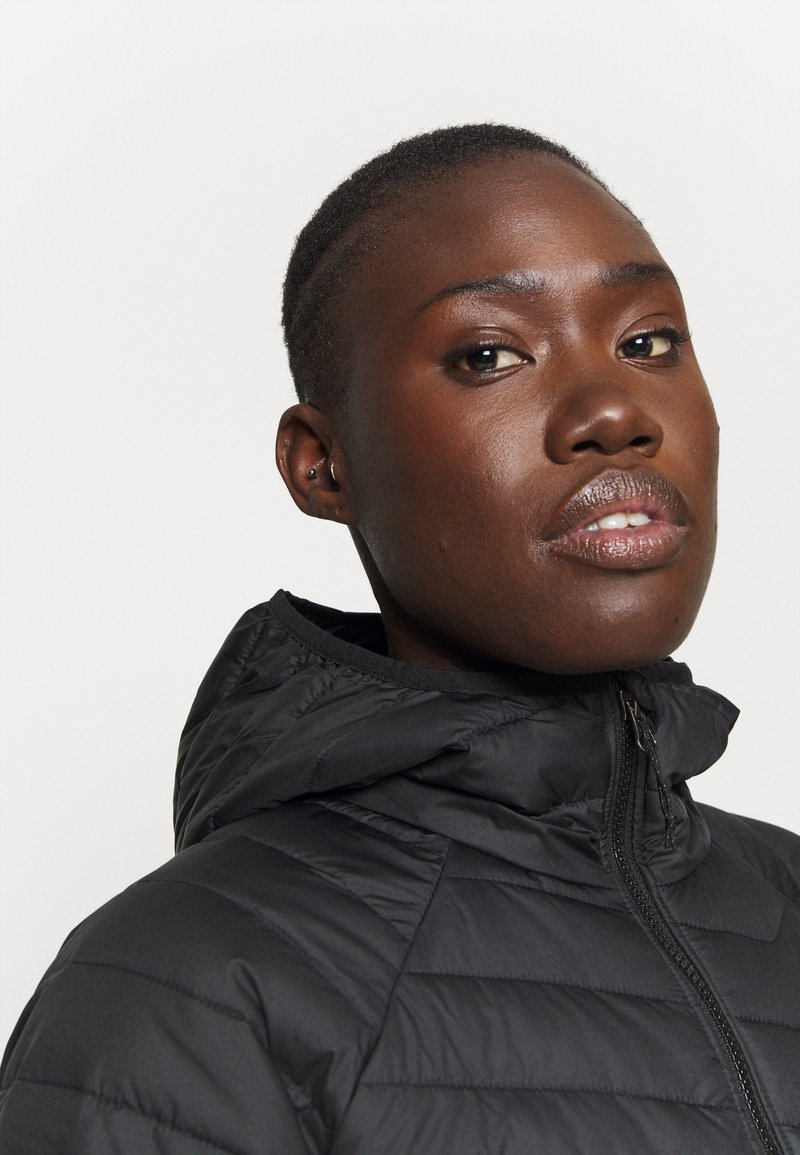 Chaqueta de plumas negra con capucha, diseño acolchado, cremallera visible y cuello alto. Textura suave y forma ajustada.