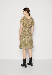 Blumenmusterkleid mit kurzen Ärmeln, V-Ausschnitt und weitem Saum. Die Farben umfassen Beige, Braun und Grün. Getragen mit schwarzen Knöchelstiefeln.