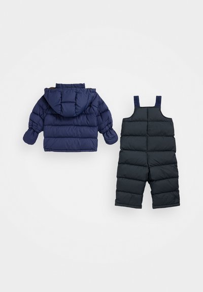 Tamsiai mėlynas pūstas kūdikių žiemos švarkas su gobtuvu ir atitinkamos juodos pūstos sniego kelnės, išdėstytos ant baltos fono.