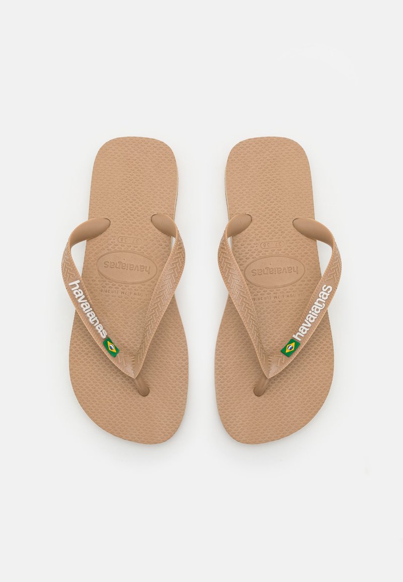 Tan spalvoti guminiai šlepetės su tekstūruotais pado paviršiais. Plonos dirželiai su baltu „Havaianas“ ženklinimu ir mažu Braziliškos vėliavos akcentu.