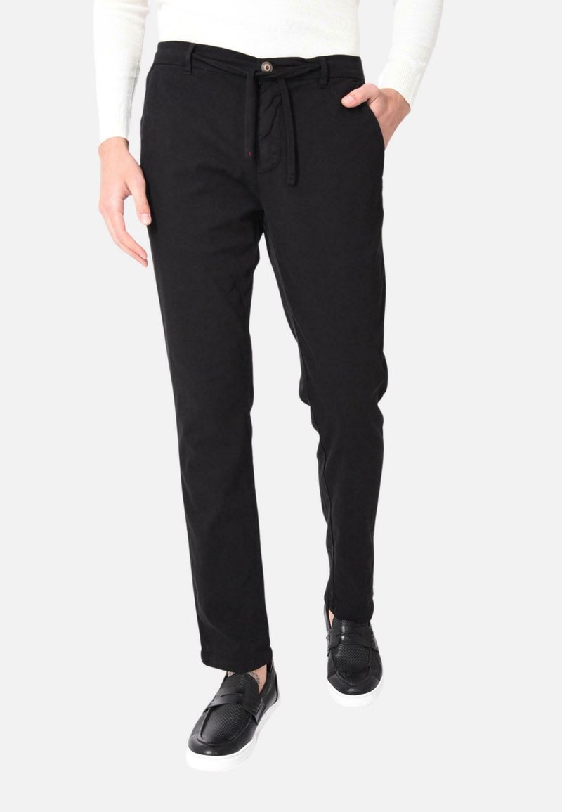 Pantaloni in cotone nero con vestibilità rilassata, vita con cordoncino e tasche laterali sottili, abbinati a scarpe slip-on nere.