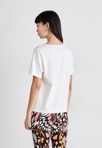 Witte t-shirt met korte mouwen en een ronde hals, met een soepele textuur. Gecombineerd met kleurrijke broek met vlinderpatroon, met roze, oranje en zwarte accenten.