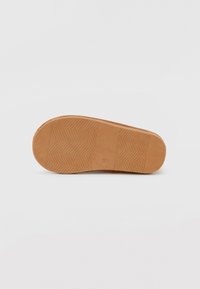 Tan gummisula med ett fiskbensmönster. Slät yta med platt form, med en liten rektangulär detalj nära hälen.