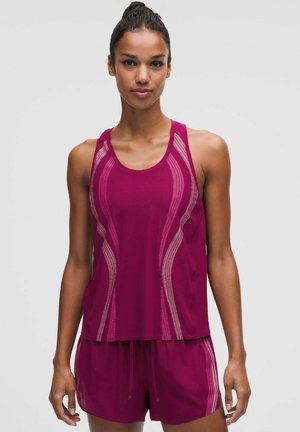 Donna in piedi, rivolta in avanti, indossa una canotta senza maniche magenta e pantaloncini abbinati con strisce ondulate rosa chiaro.