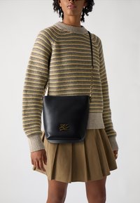 Černá kožená crossbody taška se zlatými detaily, vyznačující se hladkým povrchem a jednoduchým siluetou. Spárována s pruhovaným svetrem a skládací sukní.