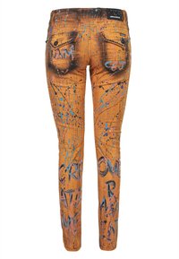 Jean skinny en denim orange avec un motif de peinture éclaboussée, mettant en avant des accents bleus et roses. Les poches arrière comportent des textes et des détails artistiques.