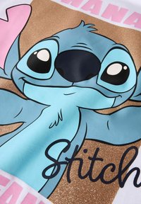 Tričko s karikaturou postavy s modrým tělem, černým nosem a velkýma očima. Pozadí je zlaté s třpytkami a textem "Stitch" v černé barvě.