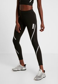 Black leggings with white side stripes and a white Puma logo, made from stretchy material. Worn with silver athletic shoes.