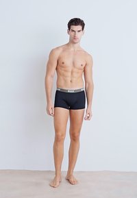 Schwarze Boxershorts mit einem dicken grauen Bund, auf dem der Text "BOSS" steht. Der Stoff wirkt glatt und hat eine figurbetonte Passform.