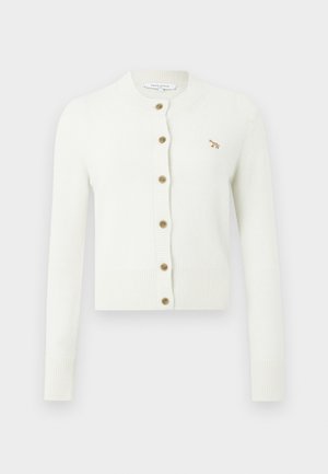 Balts adīts kardigāns ar ribotām piedurknēm un apakšmalu, ar sešu zelta pogu rindu un mazu zeltītu dzīvnieka izšuvumu uz krūtīm.