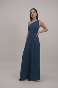 Macacão de uma só alça em azul intenso, com um corpete ajustado, design de perna larga plissada e textura de tecido suave. Sapatos de salto pretos completam o visual.