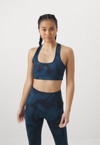 Conjunto de sujetador deportivo y leggings en verde azulado oscuro con un patrón mármol abstracto. El material parece suave con un diseño ajustado y detalles del logo en el sujetador.