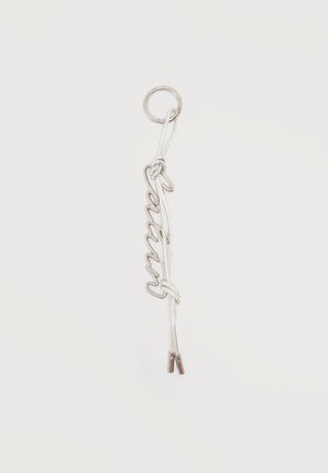 Sølvnøglevedhæng med "Queen" stavet med kursiv tråd, fastgjort til en ring og bundet med en hvid snor, der ender i metalspidser.