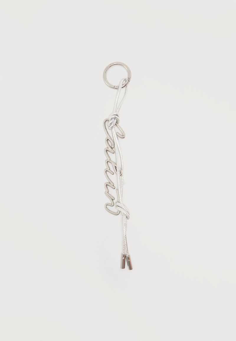 Ασημένιο μπρελόκ με τη λέξη «Queen» γραμμένη με καλλιγραφικό σύρμα, προσαρτημένο σε κρίκο και δεμένο με λευκό κορδόνι που καταλήγει σε μεταλλικές άκρες.