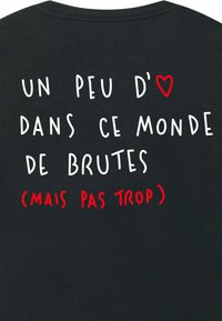 Čierne bavlnené tričko s bielym a červeným textom: "trochu ❤️ v tomto svete brutalít (ale nie príliš)." Jednoduchý, neformálny dizajn.