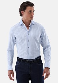 Hellblau gestreiftes Hemd mit Button-Down-Kragen, langen Ärmeln und silbernen Knöpfen. Getragen mit dunklen Jeans und einem schwarzen Gürtel.