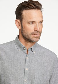 Lichtgrijs overhemd met knopen en een korte kraag, voorzak en een textuurstof; voorzien van bruine knopen en een casual ontwerp.