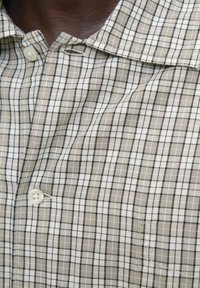 Hellbraunes kariertes Hemd mit weißen und schwarzen Gittermustern, das einen großen Kragen und einen Knopf an der Knopfleiste aufweist. Weiche Stofftextur.