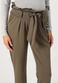 Pantalons khaki ajustés avec une ceinture froncée et une ceinture nouée. Tissu doux avec des plis, forme structurée et coupe décontractée.