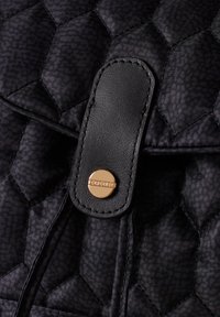 Quilted black fabric backpack with a hexagonal pattern, featuring a black leather flap and a gold-tone snap closure.