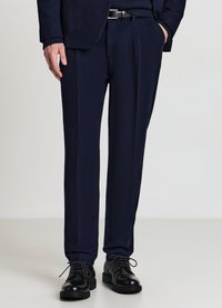 Marineblaue Wollhose mit maßgeschneiderter Passform, ausgestaltet mit Falten, Seitentaschen und glatter Textur, kombiniert mit schwarzen Lederschuhen.