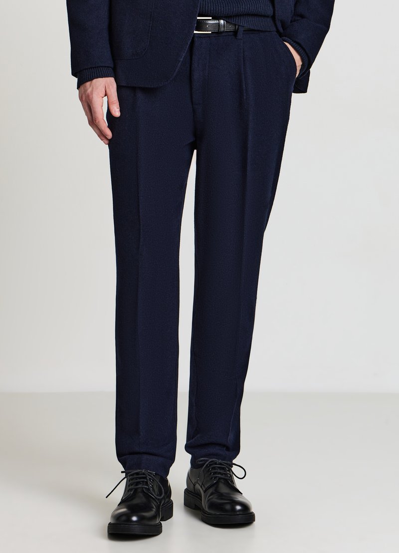 Marineblaue Wollhose mit maßgeschneiderter Passform, ausgestaltet mit Falten, Seitentaschen und glatter Textur, kombiniert mit schwarzen Lederschuhen.