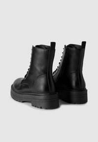 Czarne skórzane botki z wytrzymałymi, masywnymi podeszwami i sznurowanym designem. Posiadają boczny zamek błyskawiczny oraz tekstylną podszewkę zapewniającą komfort.