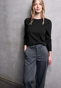 Maglione nero a maglia con maniche lunghe e dettagli sulle spalle abbinato a pantaloni ampi grigi con tasche laterali e tessuto testurizzato.