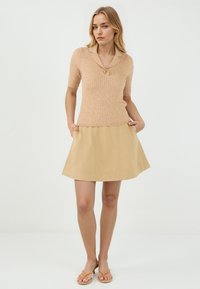 Polo à manches courtes en maille côtelée beige, associé à une jupe A-line courte de couleur beige. La jupe possède des poches latérales et un ourlet net.