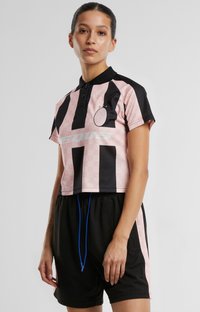 Skrajni polo z roza karo vzorcem in črnimi navpičnimi črtami. Črne kratke hlače z modrim vrvico. Diskreten detajl logotipa na prsih.