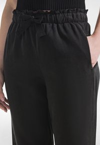 Schwarze Hose mit elastischem Bund und Knoten-Detail. Glatter Stoff, Seitentaschen und lässige Passform.