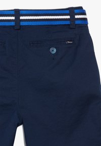 Námorně modré kraťasy s rovním předním dílem, s pruhovaným elastickým páskem v modré a bílé barvě, zadní kapsou s modrým knoflíkem a cedulkou "Polo".