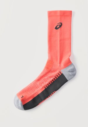 Langer korallenfarbener Sportsocken mit schwarzen und grauen Akzenten, strukturierten Griffpunkten an der Sohle und einem kleinen schwarzen Logo nahe der Bündchenkante.
