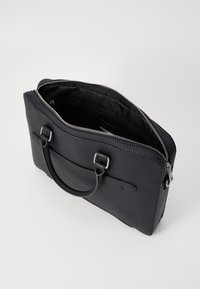 Svart läderväska med en texturerad yta, blixtlåsstängning, övre handtag och ett innertyg. Utrustad med silverfärgade detaljer.