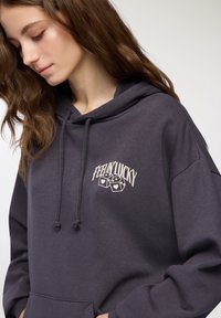 Felpa con cappuccio in tessuto grigio scuro, dotata di tasca frontale, lacci e una grafica "Feelin' Lucky" in beige chiaro con illustrazioni di dadi.