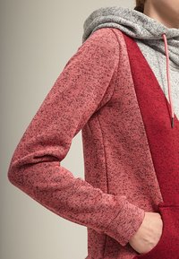 Felpa con cappuccio rossa e grigia caratterizzata da un tessuto testurizzato, una tasca a marsupio e un cappuccio con coulisse in un design a colori misti.