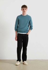 Jasnoniebieski sweter prążkowany z okrągłym dekoltem, w zestawieniu z czarnymi spodniami i beżowymi trampkami. Prosty design z delikatnym logo na swetrze.