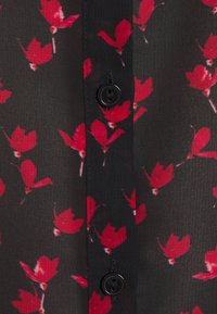 Tissu noir avec motif floral rouge, doté d'une fermeture à boutons et d'une texture légère. Remarquable pour son apparence délicate et transparente.