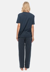 T-shirt in cotone blu navy con maniche corte abbinato a pantaloni da pigiama a righe. I pantaloni presentano righe verticali bianche e una vestibilità ampia.
